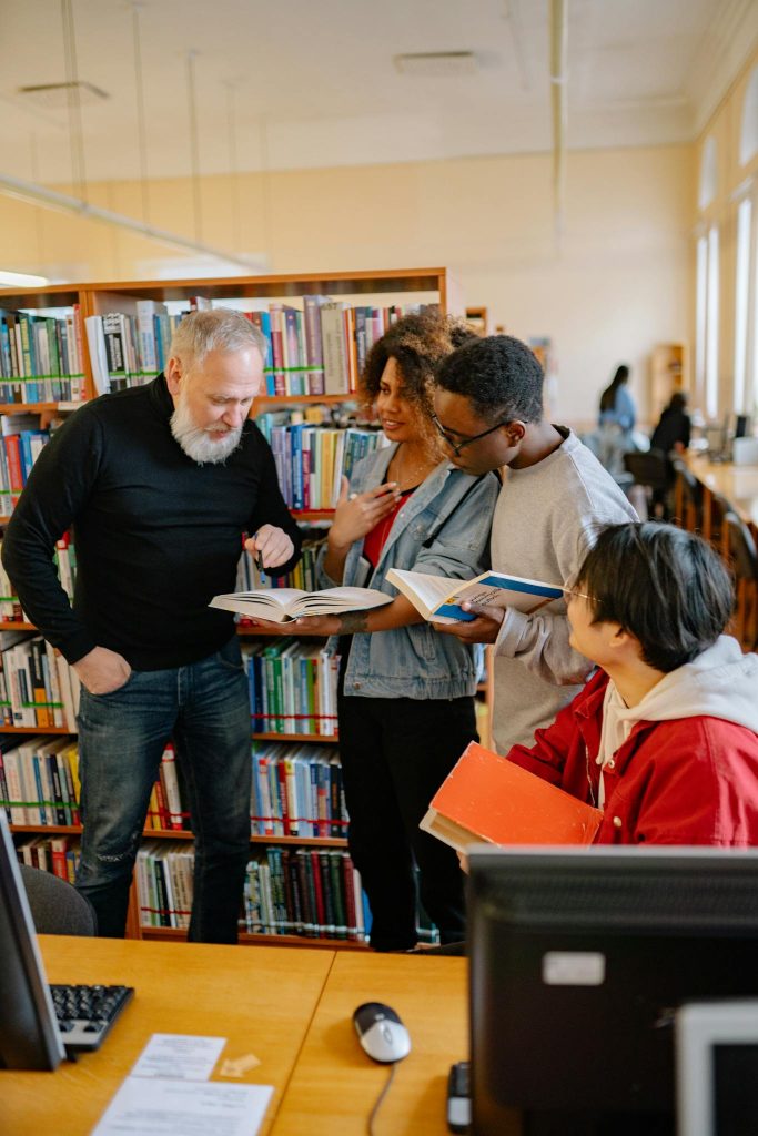 Four diverse students engaged in a collaborative study session in a library setting.
